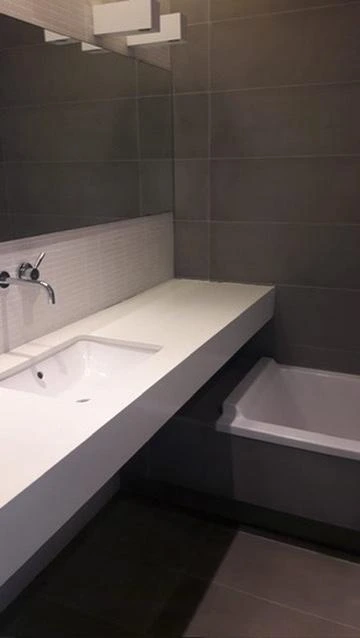 Reforma de baño con encimera volada blanca, grifería empotrada y revestimiento gris en Barcelona