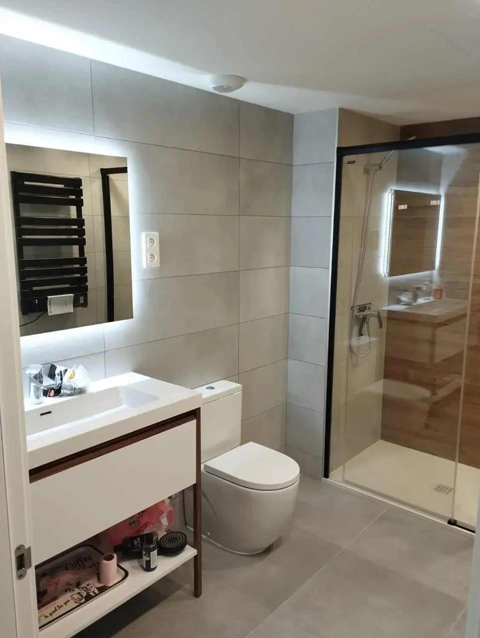 Reforma de baño con espejo retroiluminado, mampara de perfilería negra y azulejos grises en Barcelona
