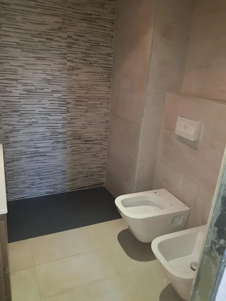 Reforma de baño con inodoro suspendido, plato de ducha de pizarra y alicatado texturizado en Barcelona