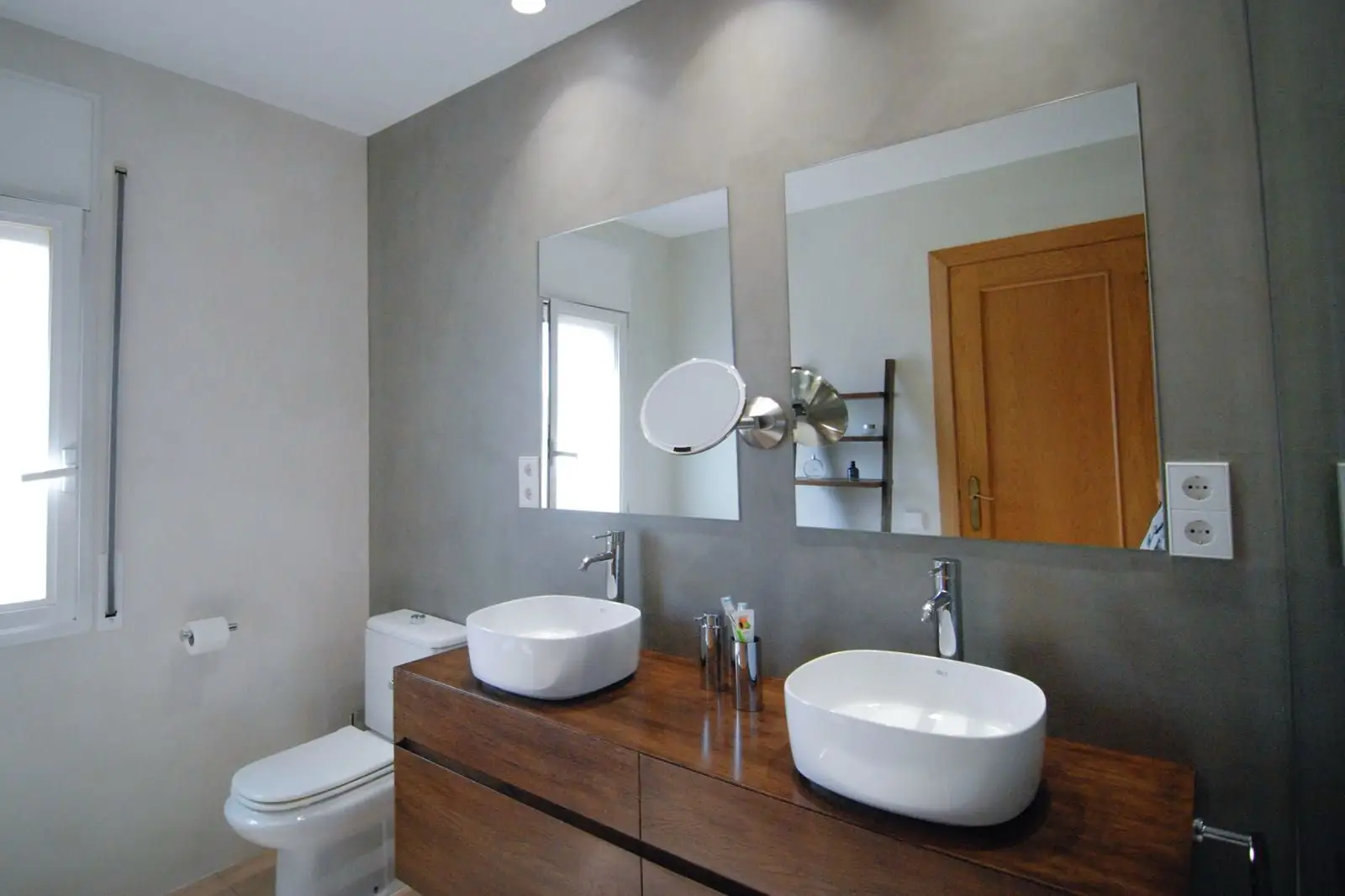 Reforma de baño con lavabo doble sobre mueble de madera y pared de microcemento en Barcelona