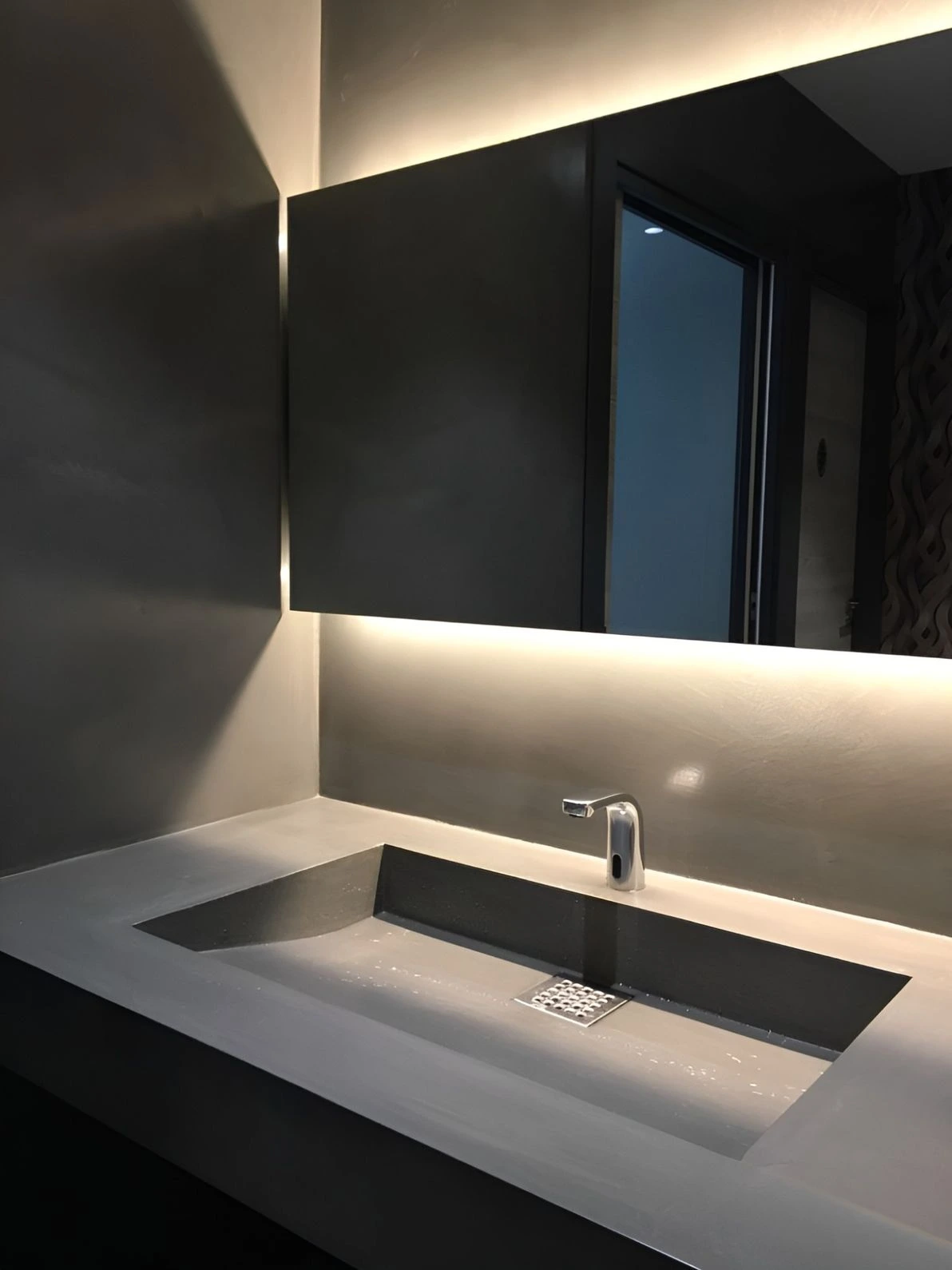 Reforma de baño con lavabo integrado de microcemento gris y espejo retroiluminado en Barcelona
