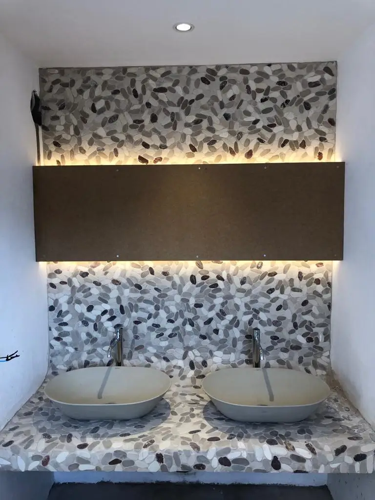 Reforma de baño con lavabos sobre encimera de piedra y pared de cantos rodados en Barcelona